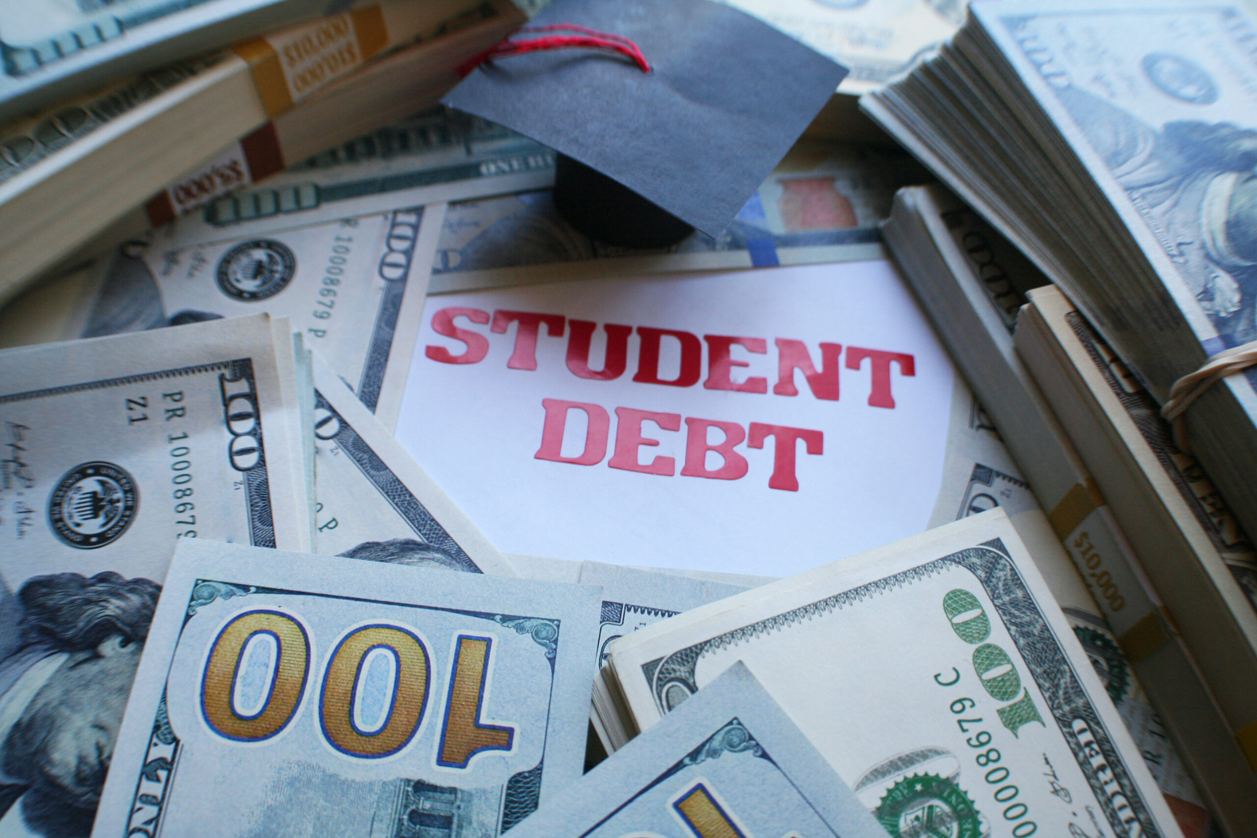 Graduation cap resting on stacks of cash beside a "Student Debt" note — can student loans be discharged in bankruptcy, Merna Law Virginia
